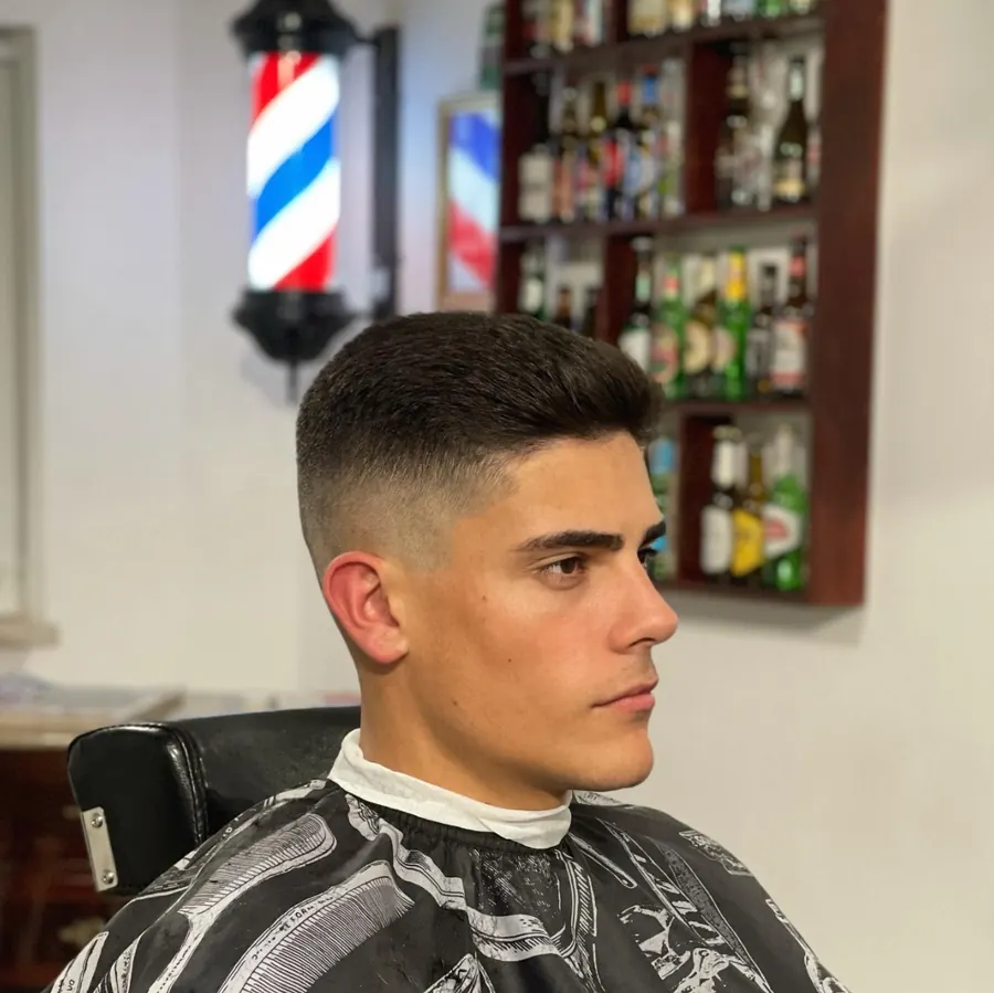 Corte skin fade com o topo curto e texturizado, visto de perfil na cadeira da Barbearia Caramujo