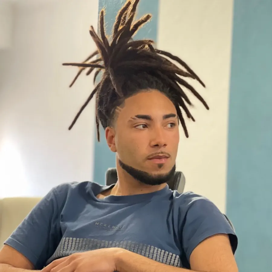 Dreads apanhadas no alto da cabeça, com risco desenhado na lateral e barba contornada